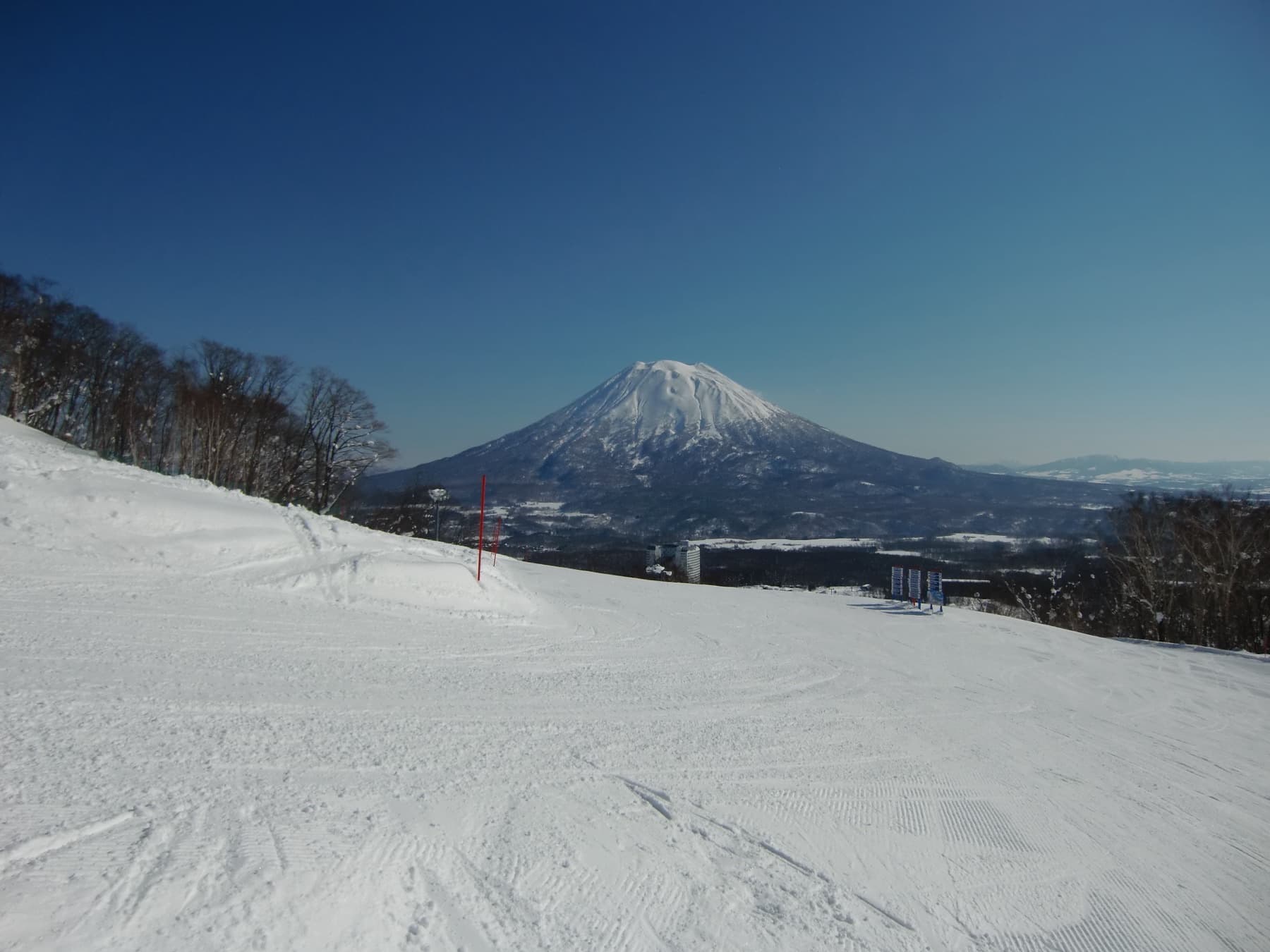 Groomed ski run in Niseko Village looking toward snow-covered Mount Yotei under a clear blue sky