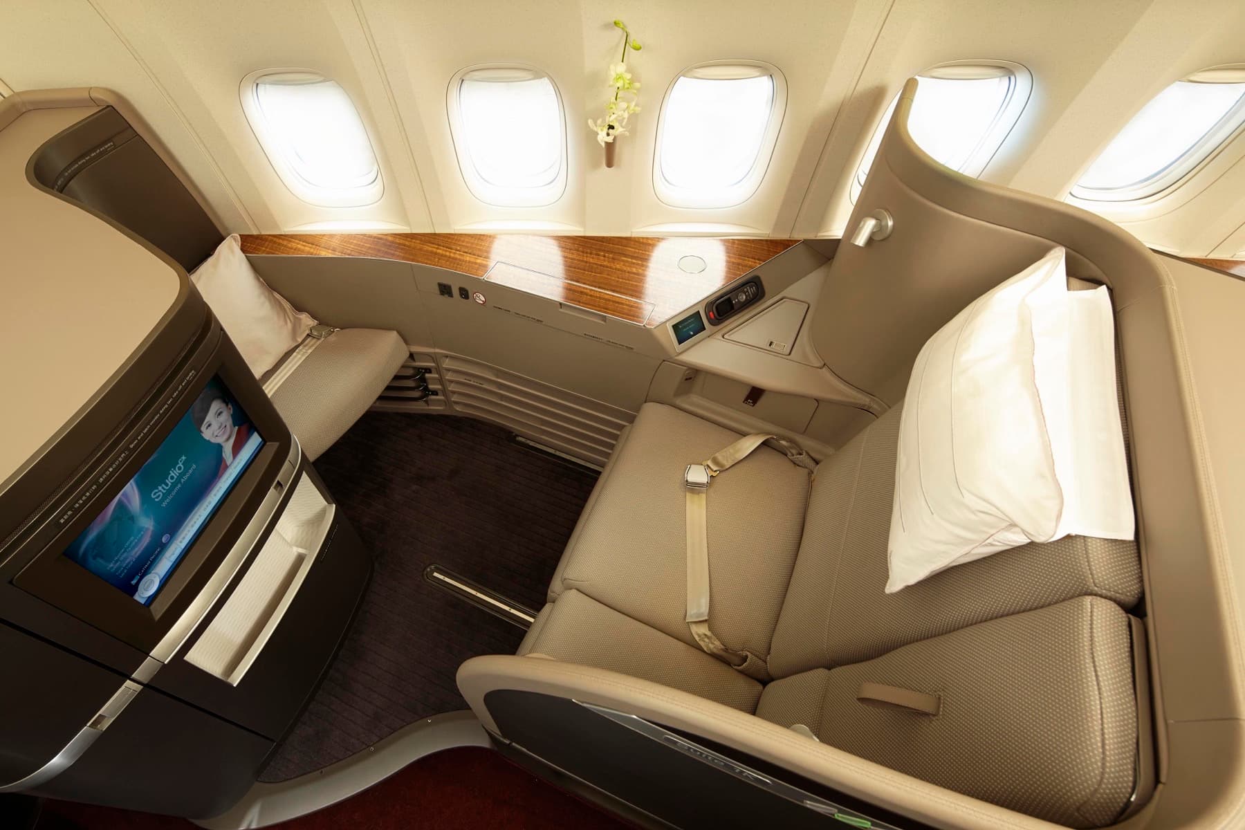 Cathay Pacific First Class suite with a wide leather seat, side table, and personal screen lit in soft cabin light