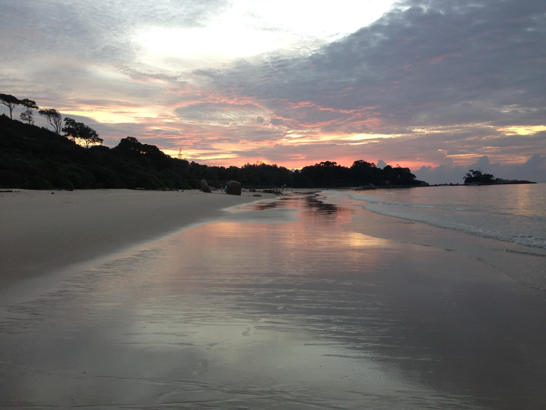 Sunset over wet sand and shallow surf on an empty beach in northern Bintan, Indonesia