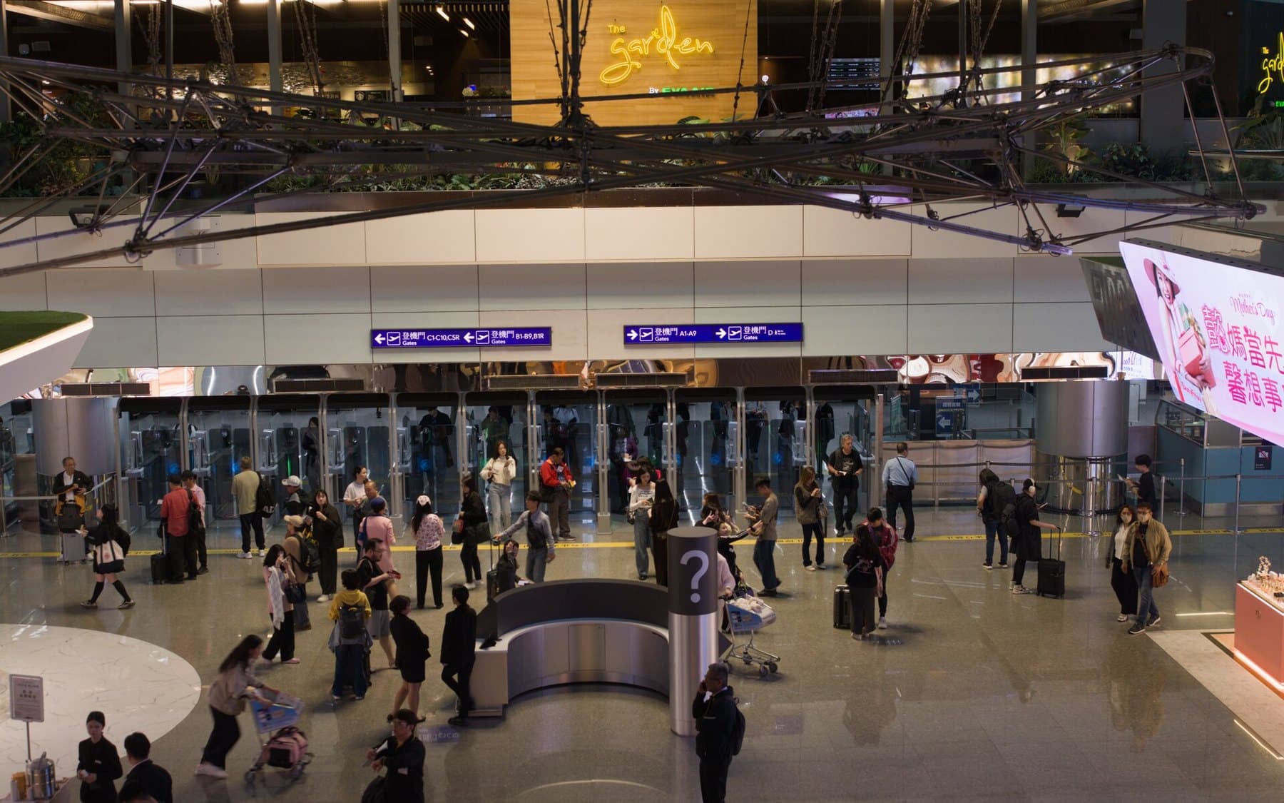 Travelers with luggage in the departure hall of Taoyuan Airport Terminal 2, under a wooden sign for The Garden