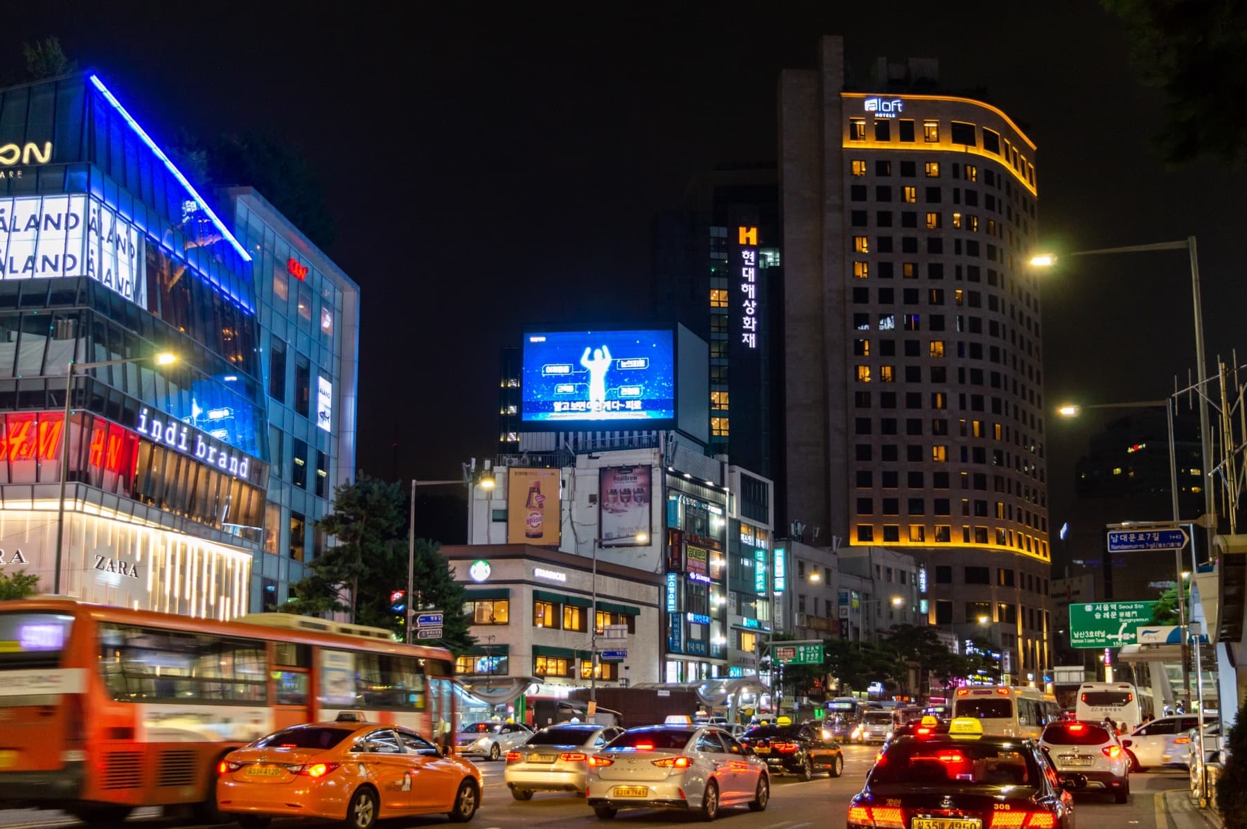 Night traffic on Namdaemun-ro in Seoul’s Myeongdong district, with taxis, a city bus, and lit hotel and shop fronts