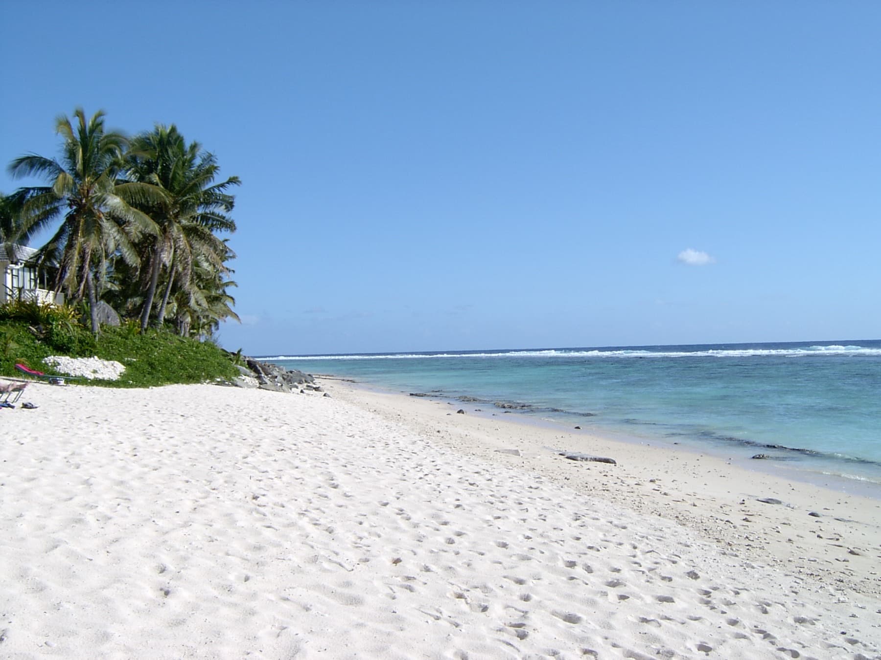 White sand and turquoise lagoon along the Arorangi coast of Rarotonga, Cook Islands, with palms and a beachfront building