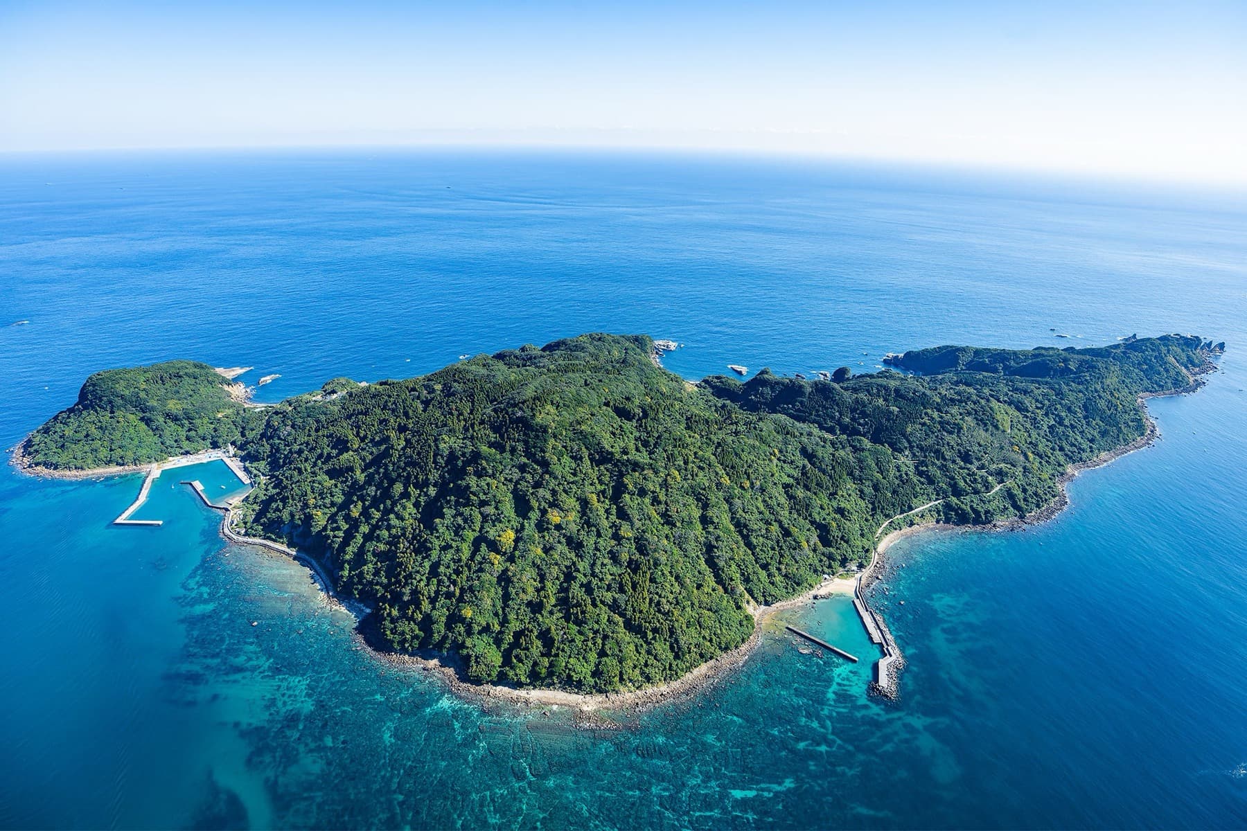 Aerial view of forested Ōshima island off Nichinan, Miyazaki, with turquoise shallows and deep Pacific blue — A Depopulated Miyazaki Island Soft-Opens as a Seven-Villa Pacific Resort