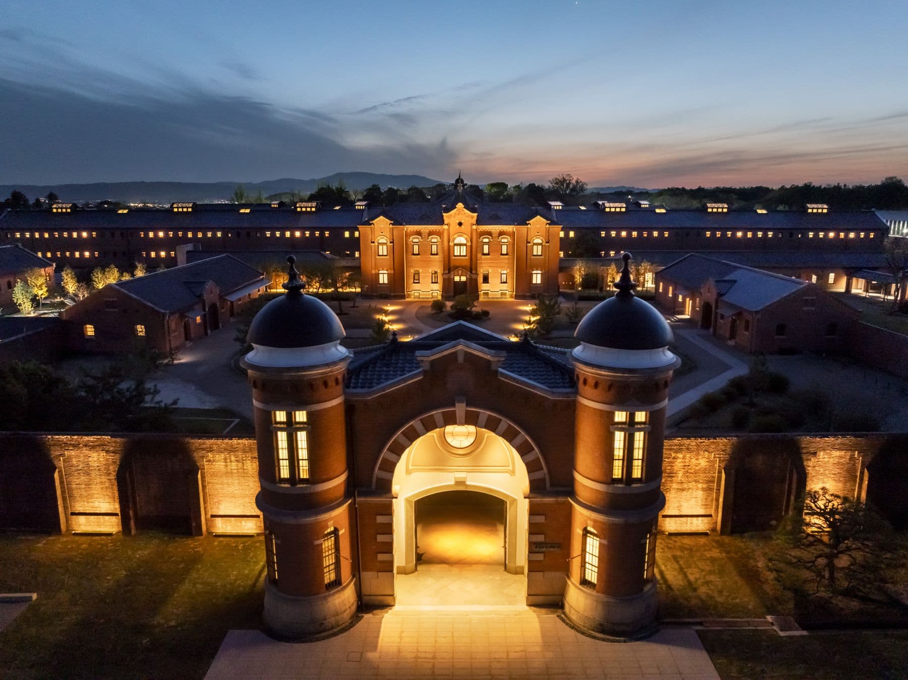 Twilight aerial of the Former Nara Prison’s red-brick main gate and illuminated radial wings, now HOSHINOYA Nara Prison — Inside the 118-Year-Old Japanese Prison Reborn as a Luxury Hotel