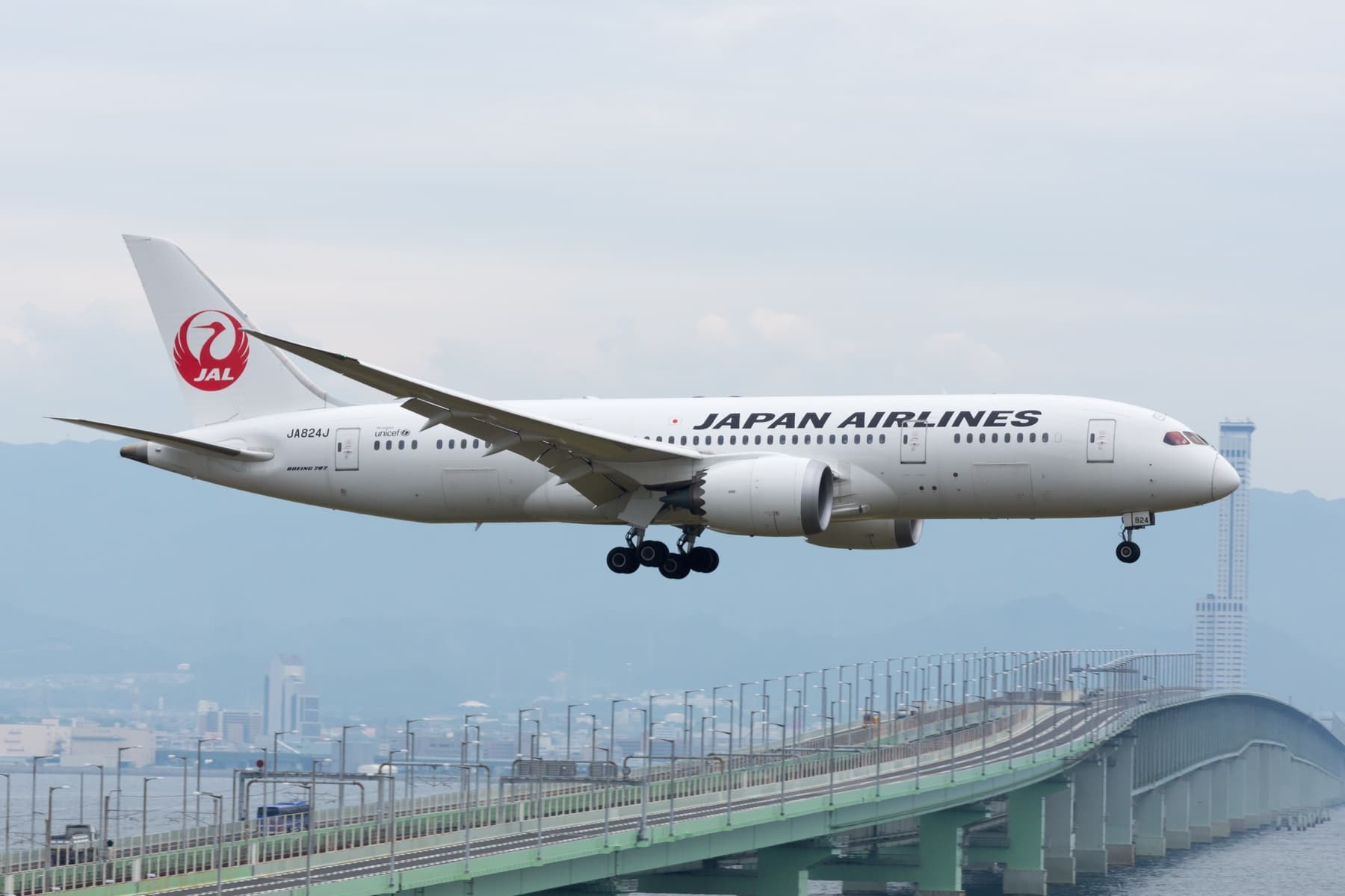 A Japan Airlines Boeing 787 on approach over a green bridge, landing gear down