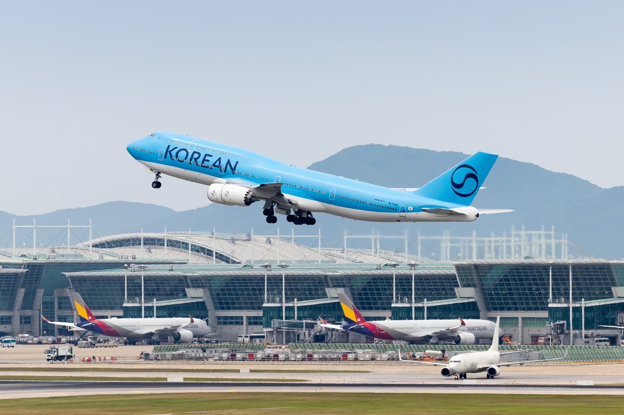 A Korean Air Boeing 747-8i climbs out of Incheon as Asiana widebodies sit at the terminal gates