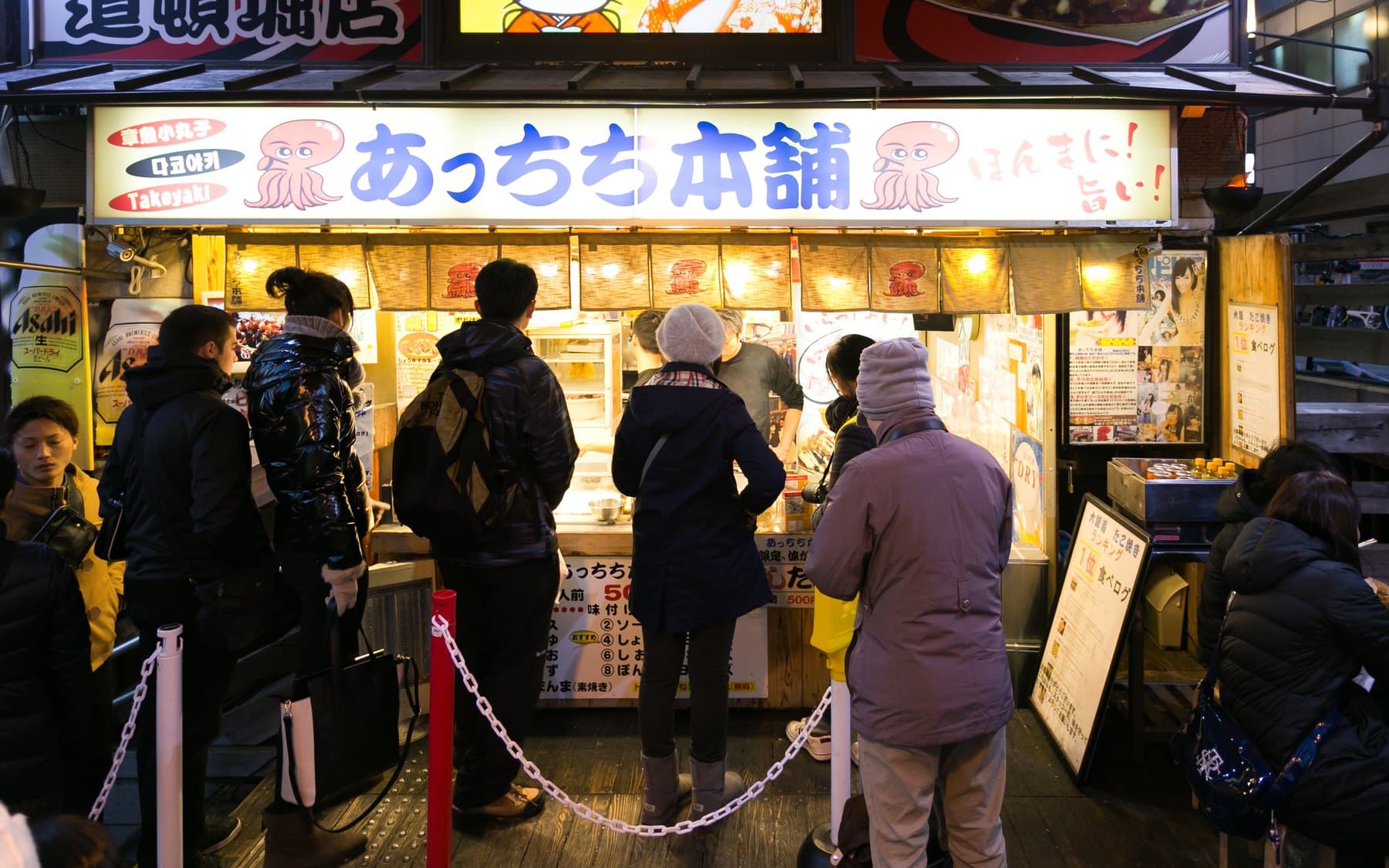 A nighttime line at a takoyaki stall under a bright octopus sign in Dotonbori