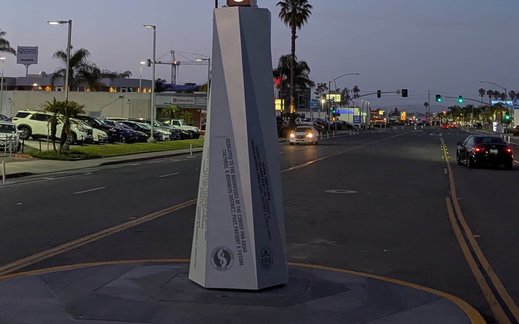 The base of the Convoy gateway sign at dusk in Kearny Mesa, with a full parking lot across the street