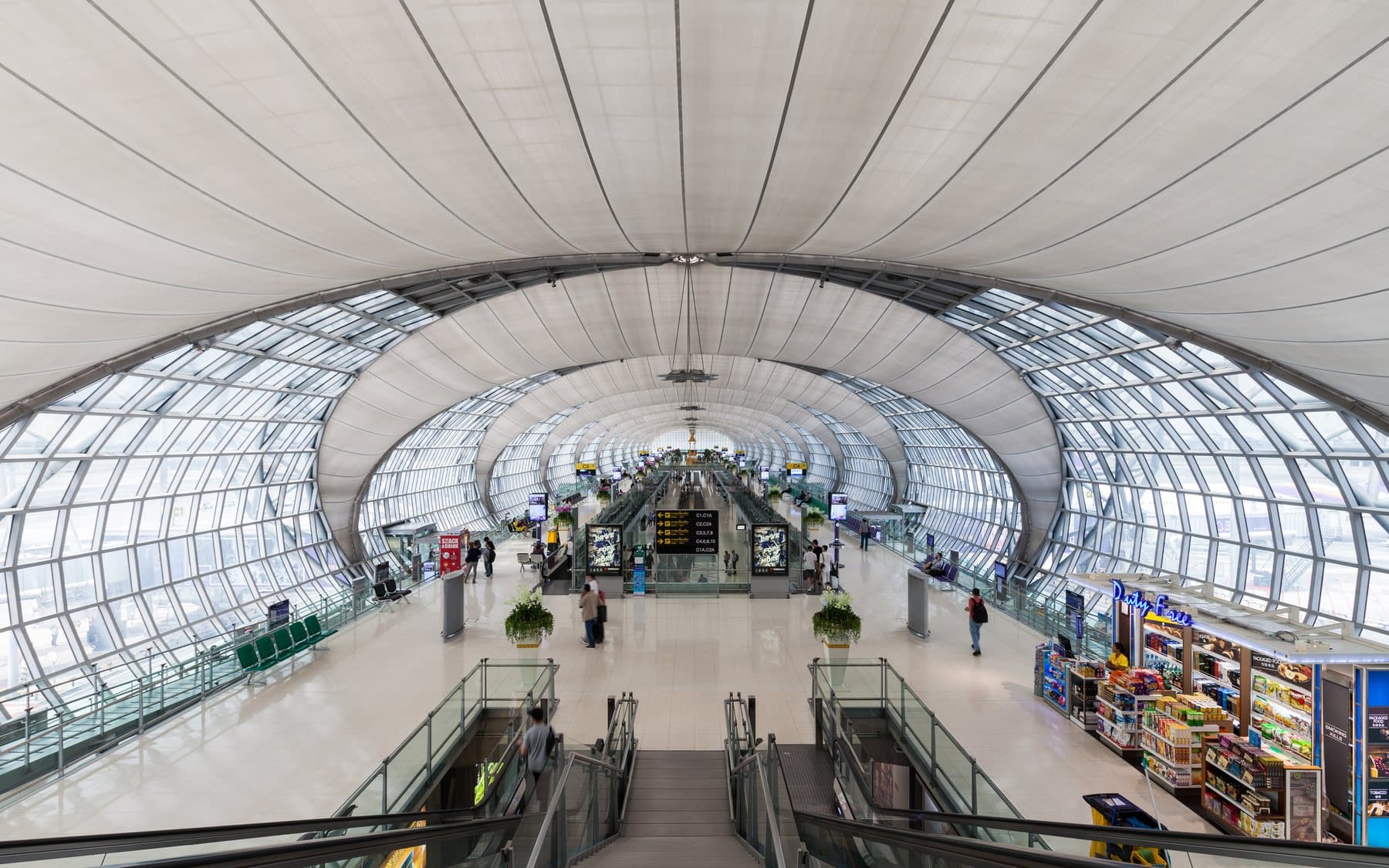 The curved glass hall of Suvarnabhumi Airport in Bangkok, seen from an upper stair toward the departure gates