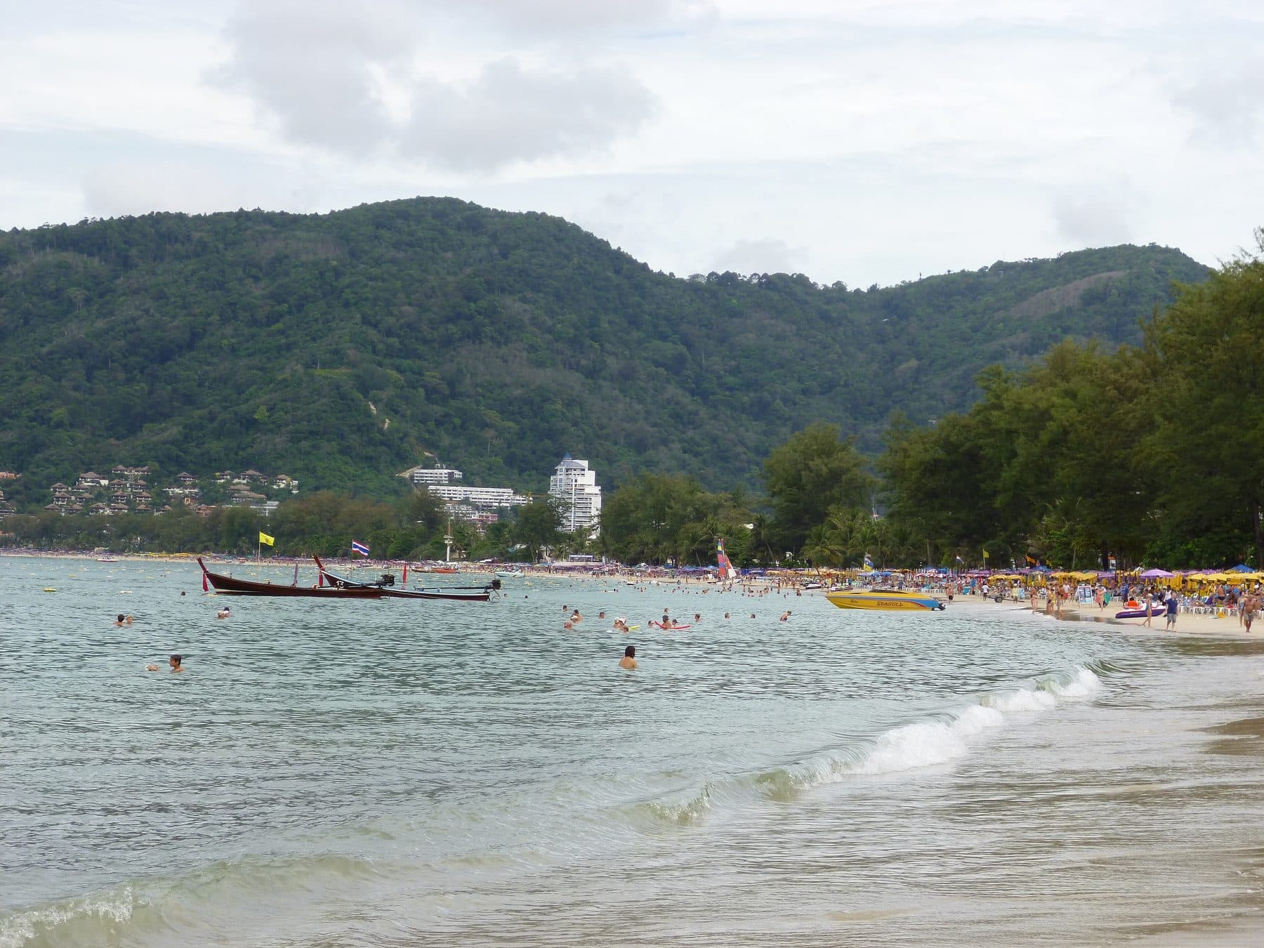 Patong Beach in Phuket with long-tail boats, umbrellas, and forested hills — Flying to Asia for Work? How to Turn a Business Trip Into a Smarter Extended Stay