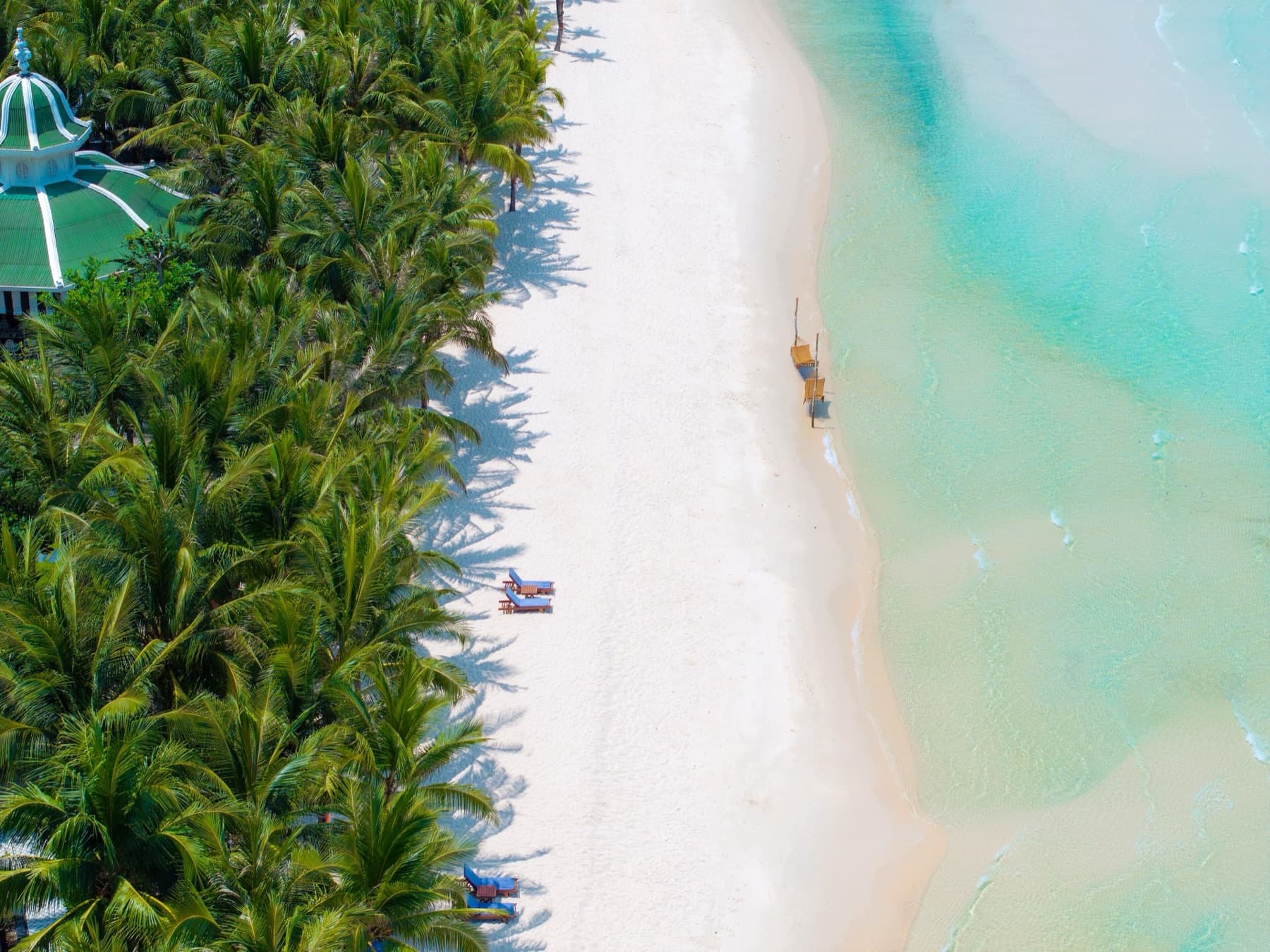 Aerial view of Kem Beach on Phu Quoc Island, with white sand, turquoise water, and palm canopy along a resort shoreline