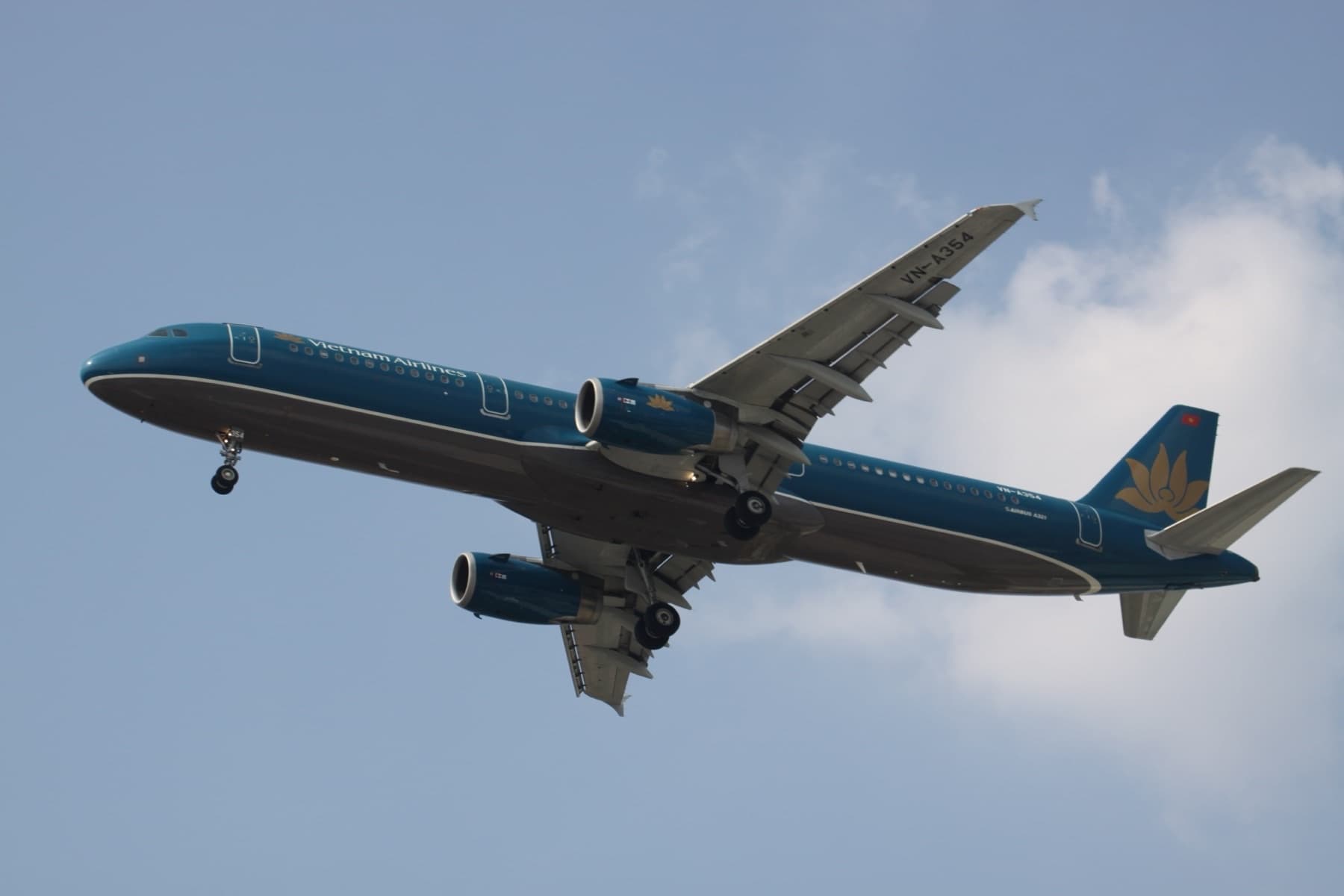 Vietnam Airlines Airbus A321 VN-A354 in teal lotus livery banking against a pale blue sky with landing gear down