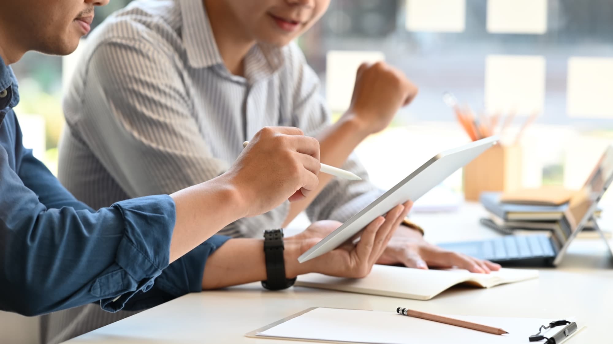 Two colleagues leaning over a tablet together at a bright workspace table