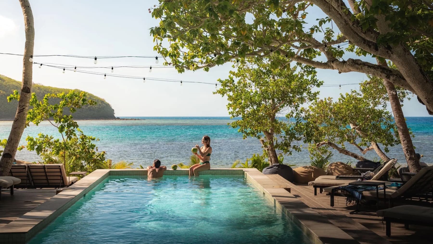 Travelers beside a pool overlooking a turquoise lagoon and green island shoreline in Fiji